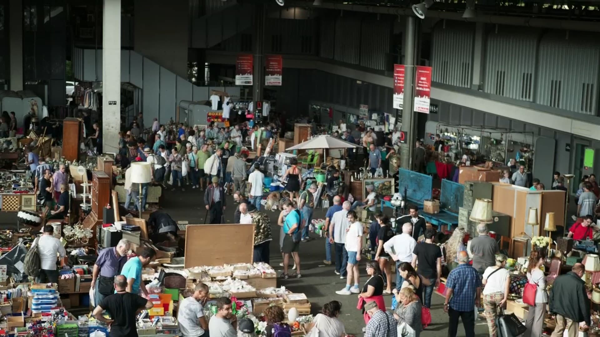A daylit, busy indoor flea market with stalls of vintage goods and second-hand treasures as shoppers browse
